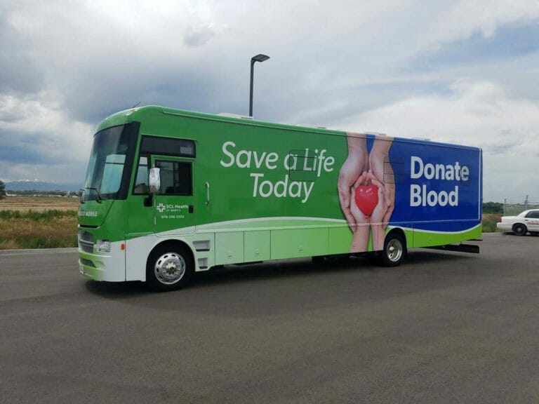 Bloodmobile parked outside. Side of the bloodmobile has text that says