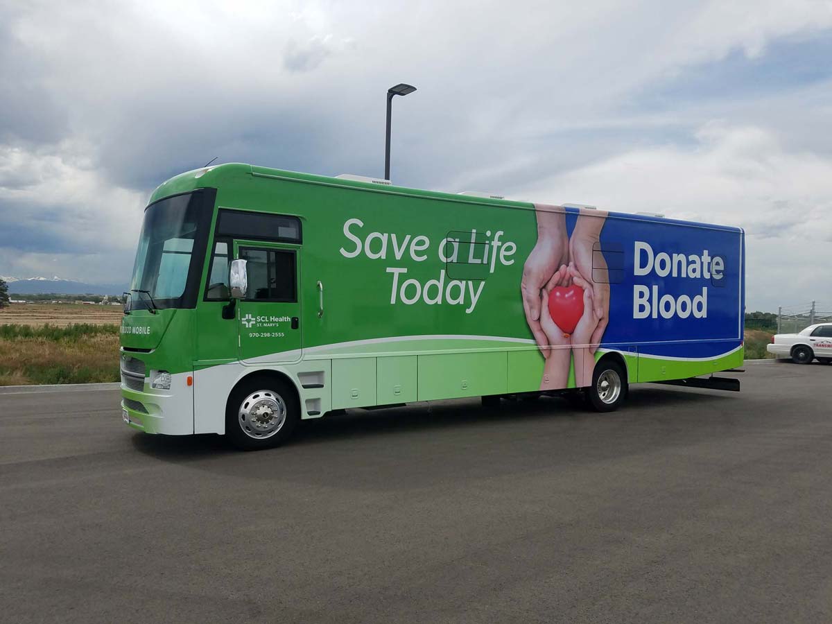 Bloodmobile parked outside. Side of the bloodmobile has text that says